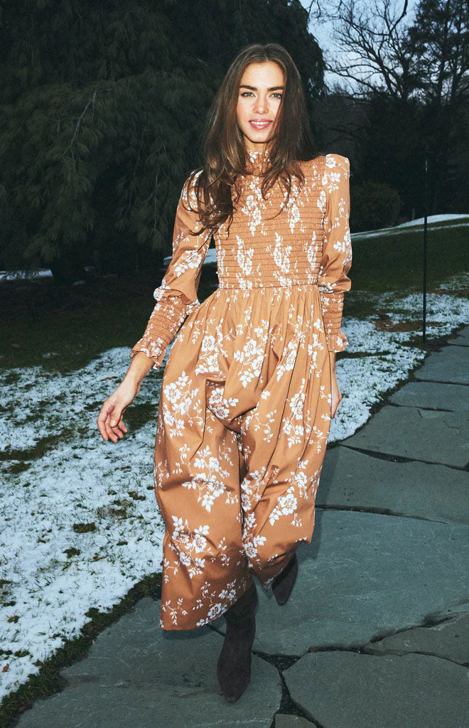 Front view of Molly dress with smocked high neck, long sleeves, and midi skirt in burnt orange floral on a snowy path