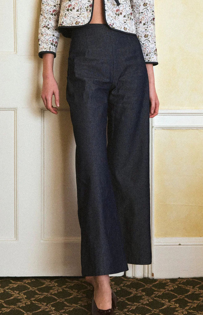 Front view of Elise Pant in denim on model highlighting high-rise, wide-leg silhouette against a cream paneled wall