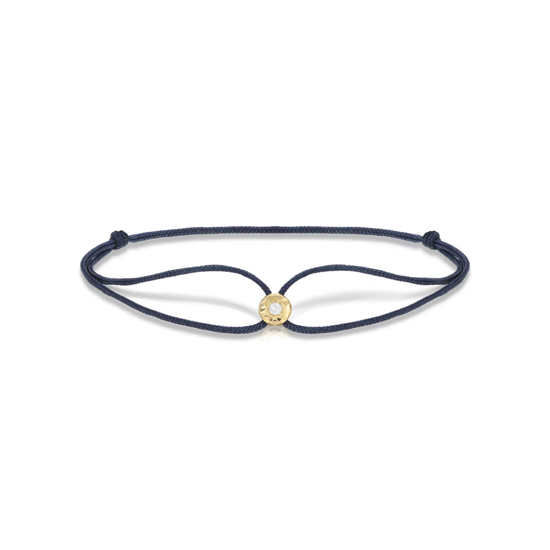 Top view of navy parachute bracelet showing adjustable navy cord and gold bezel with clear gem on white background