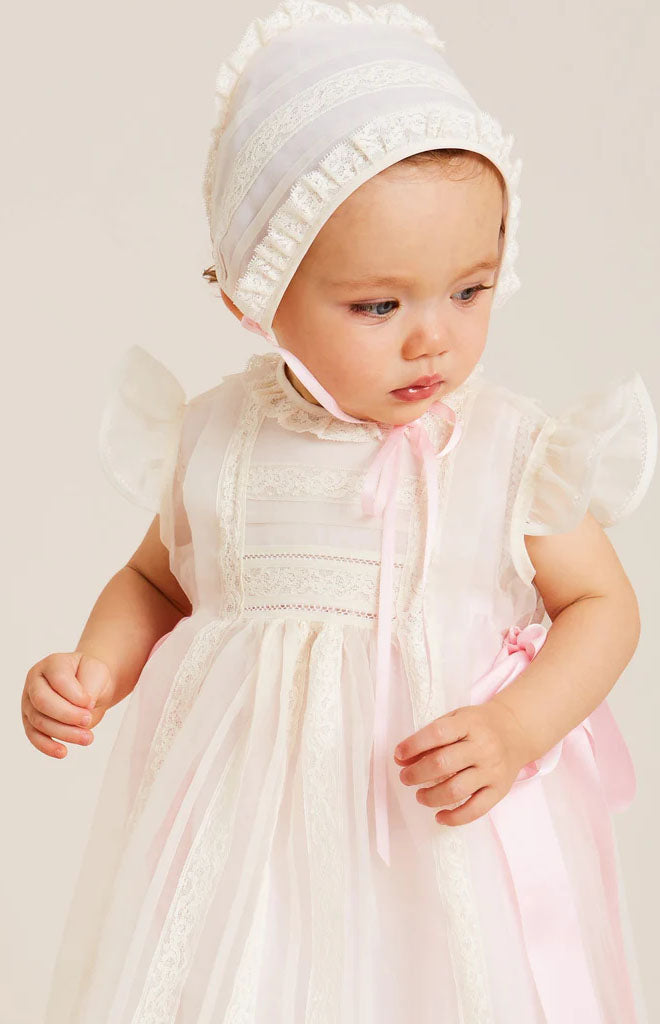 Front view of traditional light-pink christening gown on baby, showing frill sleeves, lace panel and pink ribbon sash
