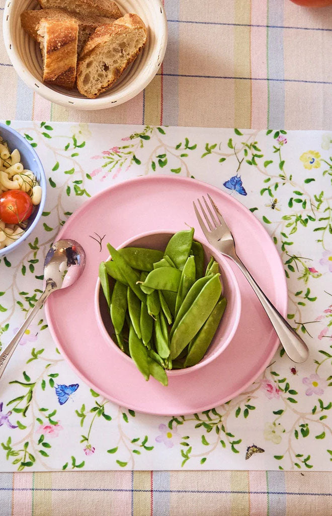 Stainless steel child-sized fork resting on a pink plate beside a spoon and bowl of snap peas on a floral placemat