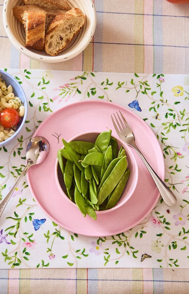 Top view of the Complete Dinnerware Set in Pink showcasing a pink plate and bowl with vegetables on a floral tablecloth