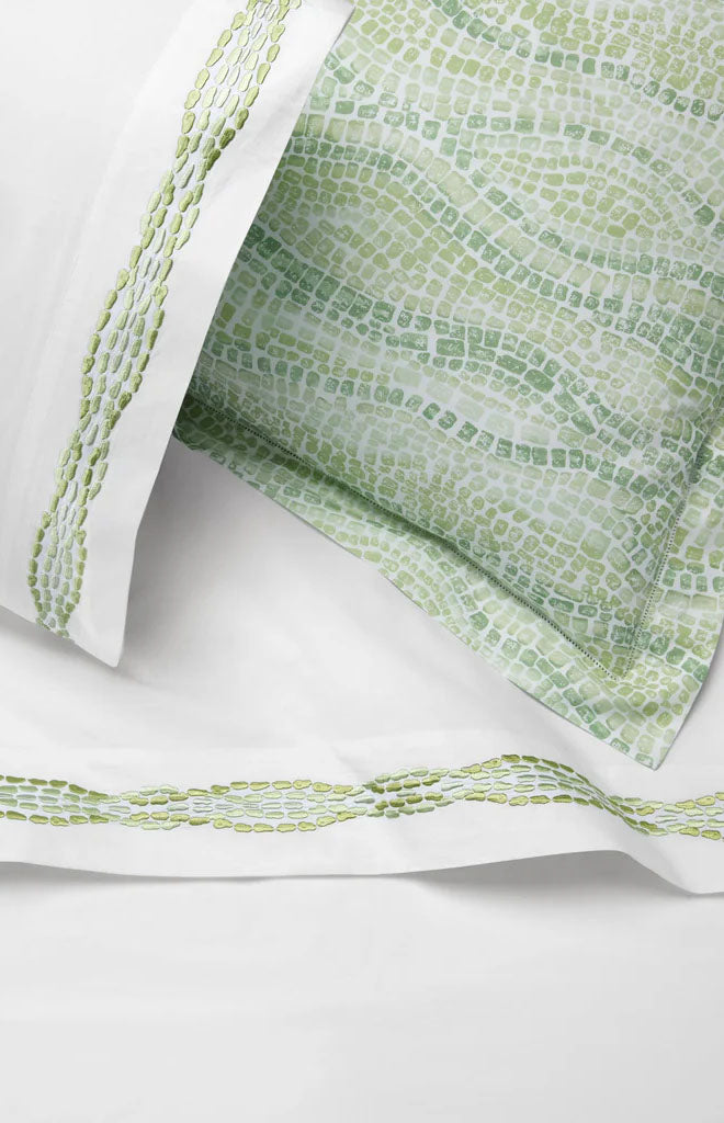 Close-up of Cobblestones flat sheet and pillowcase showing green watercolor mosaic print and embroidered green border on white background