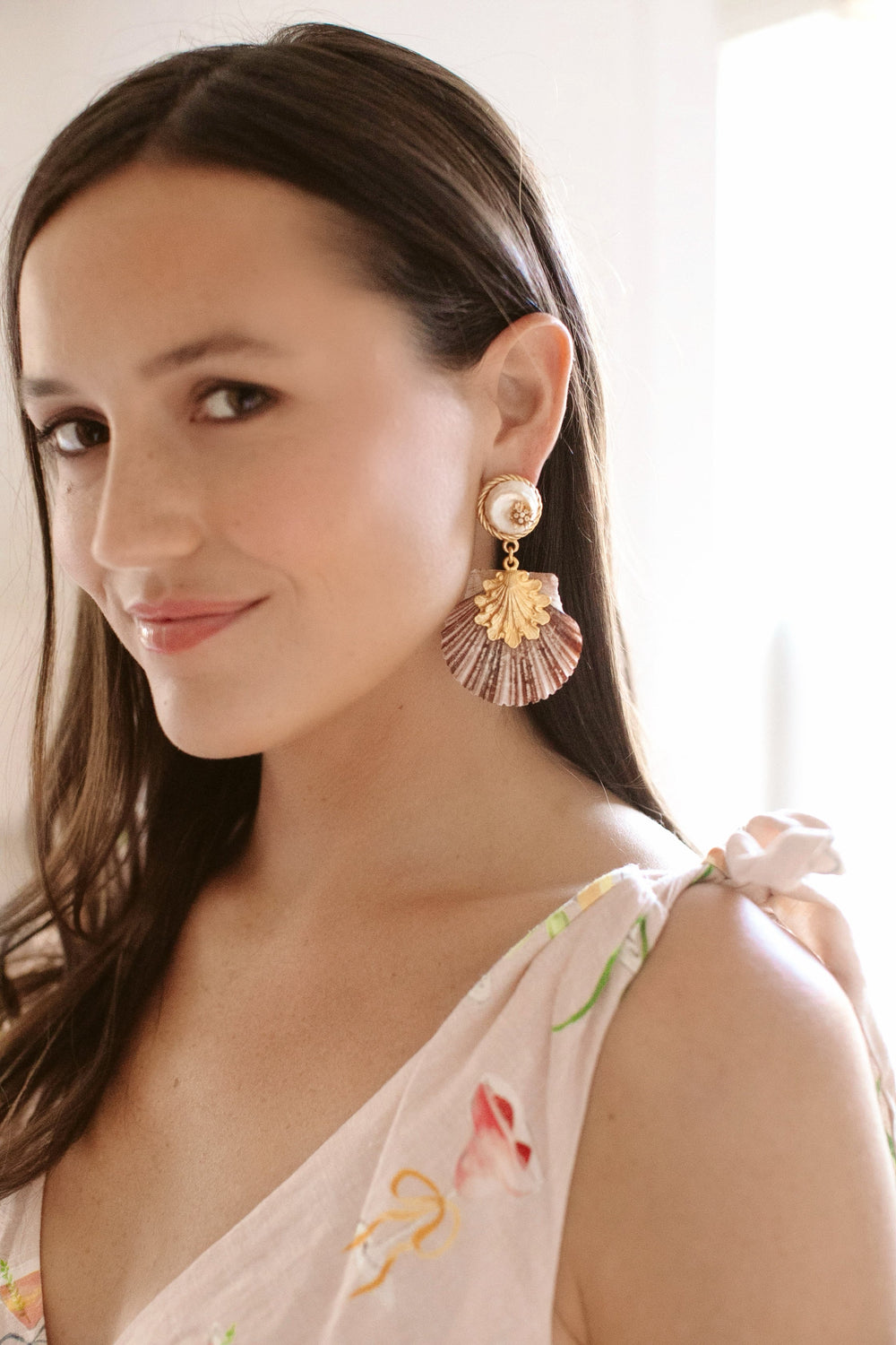 Woman wearing gold-toned shell drop earrings in a soft-lit indoor portrait