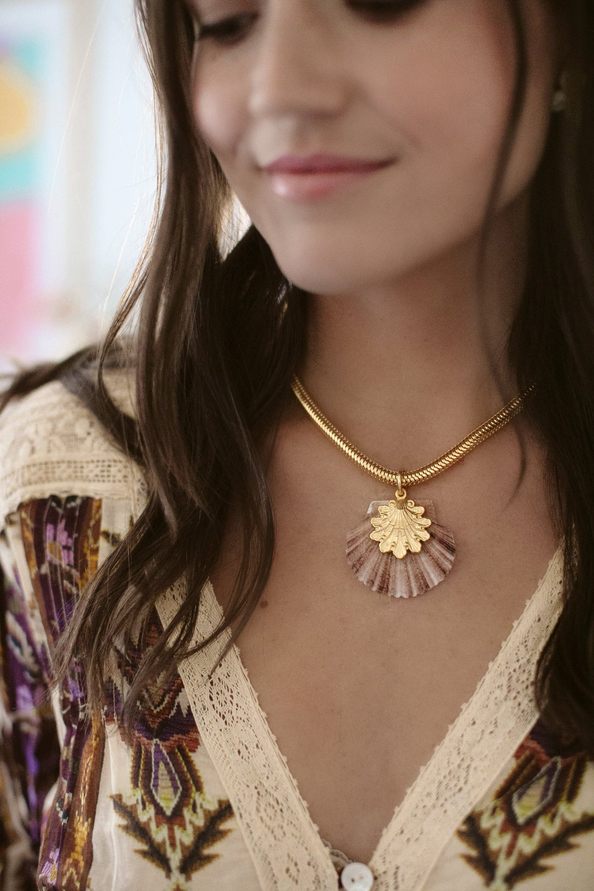 Close-up of Oceana Necklace on model showcasing a baby scallop shell pendant with 24K antique gold plating on a gold snake chain, soft indoor background