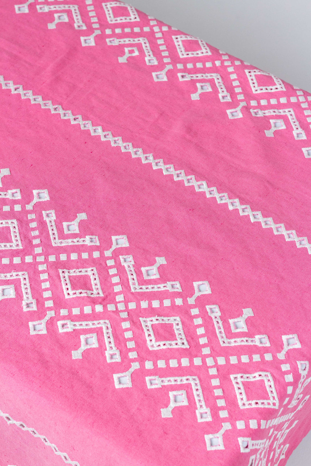 Close-up of Ojete rectangular tablecloth showing white embroidered eyelet geometric pattern on bougainvillea pink fabric