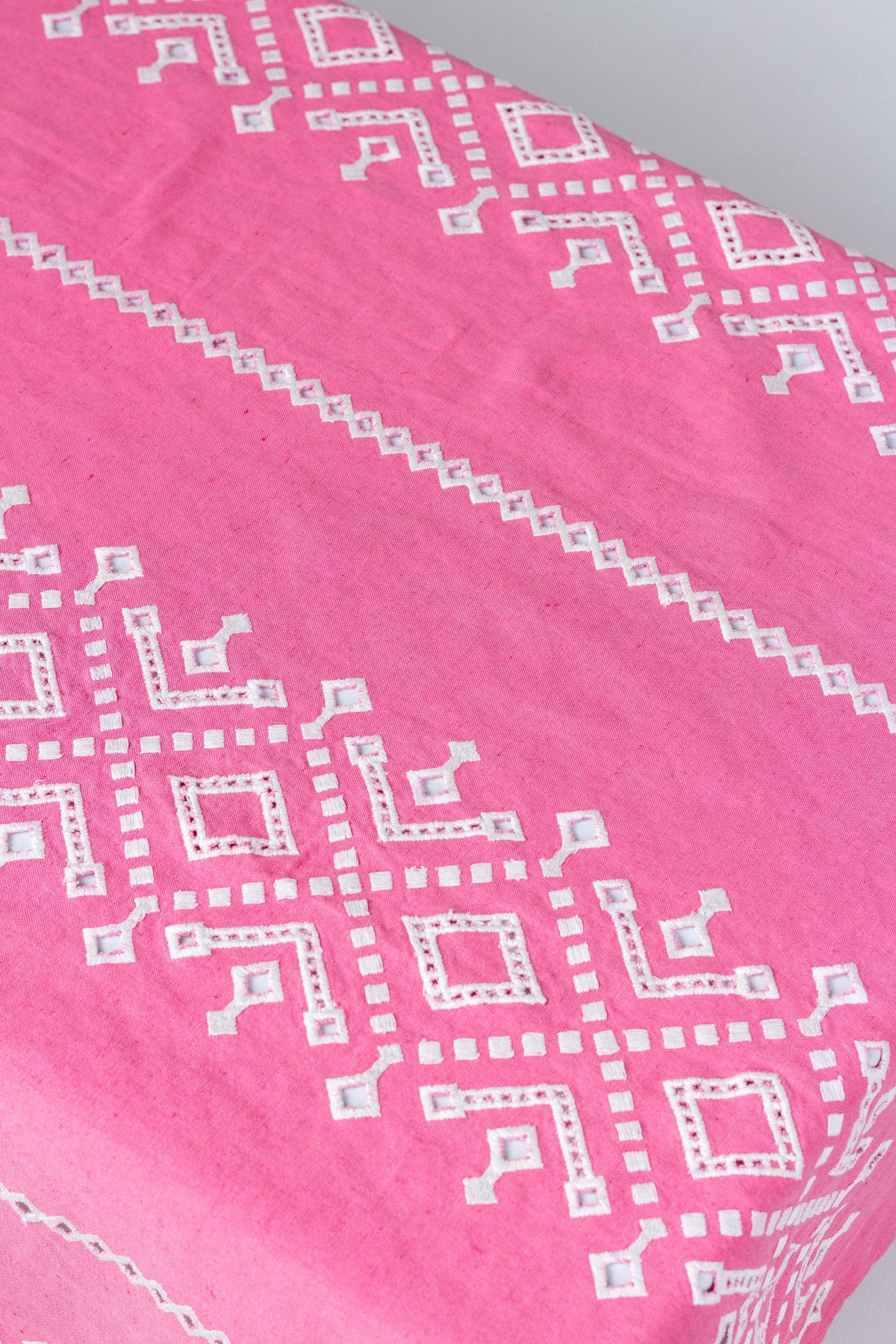 Close-up of Ojete rectangular tablecloth showing white embroidered eyelet geometric pattern on bougainvillea pink fabric