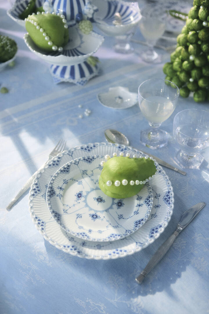 Top-down view of Blue Fluted Full Lace Plate 7.5-inch showcasing hand-pierced lace rim and blue floral decoration on a light blue tablecloth