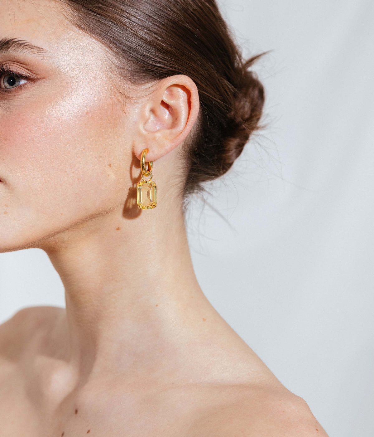 Close view of Over the Rainbow Earring Set showcasing a yellow glass charm on a 24K gold hoop against a model’s ear