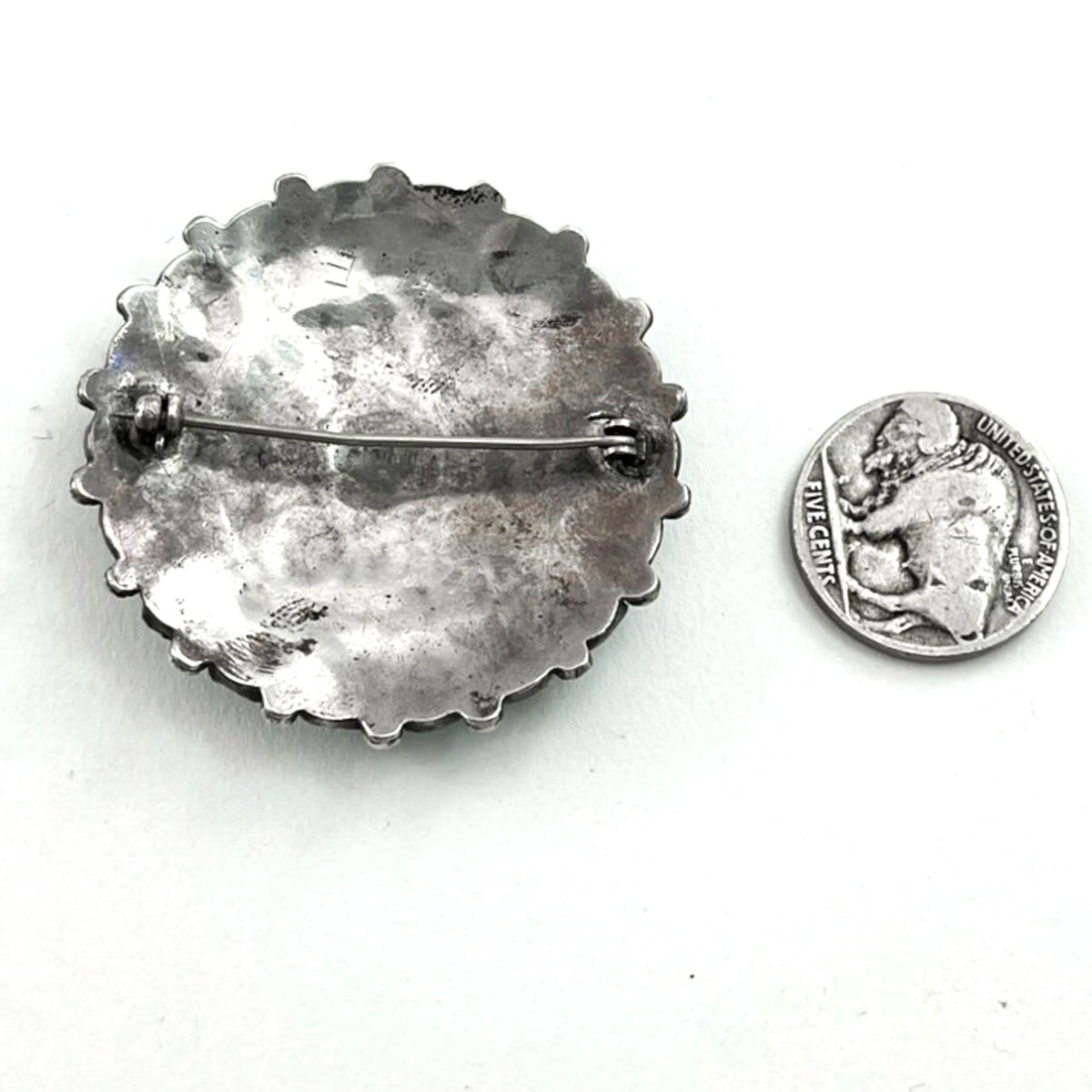 Back view of vintage sterling silver cluster pin showing its pin clasp and scalloped edge with a white background