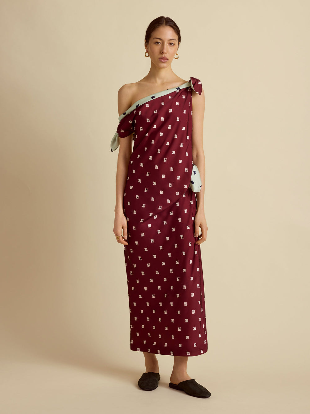 Front view of Floral Tabard Tie Dress in rosso levanto with asymmetrical one-shoulder neckline and shoulder tie on beige background