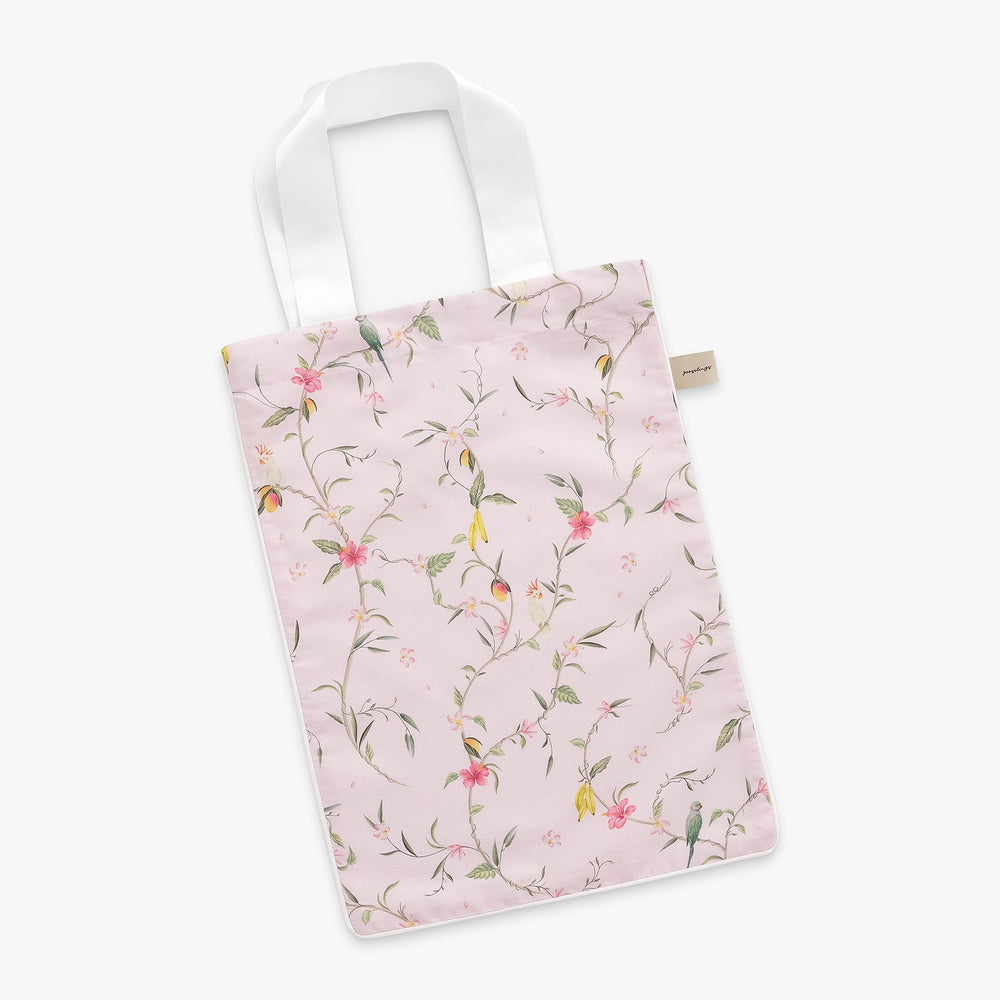 Angled flat lay of Dreaming of Paradise tote bag showcasing pink floral print and white shoulder handles on white background