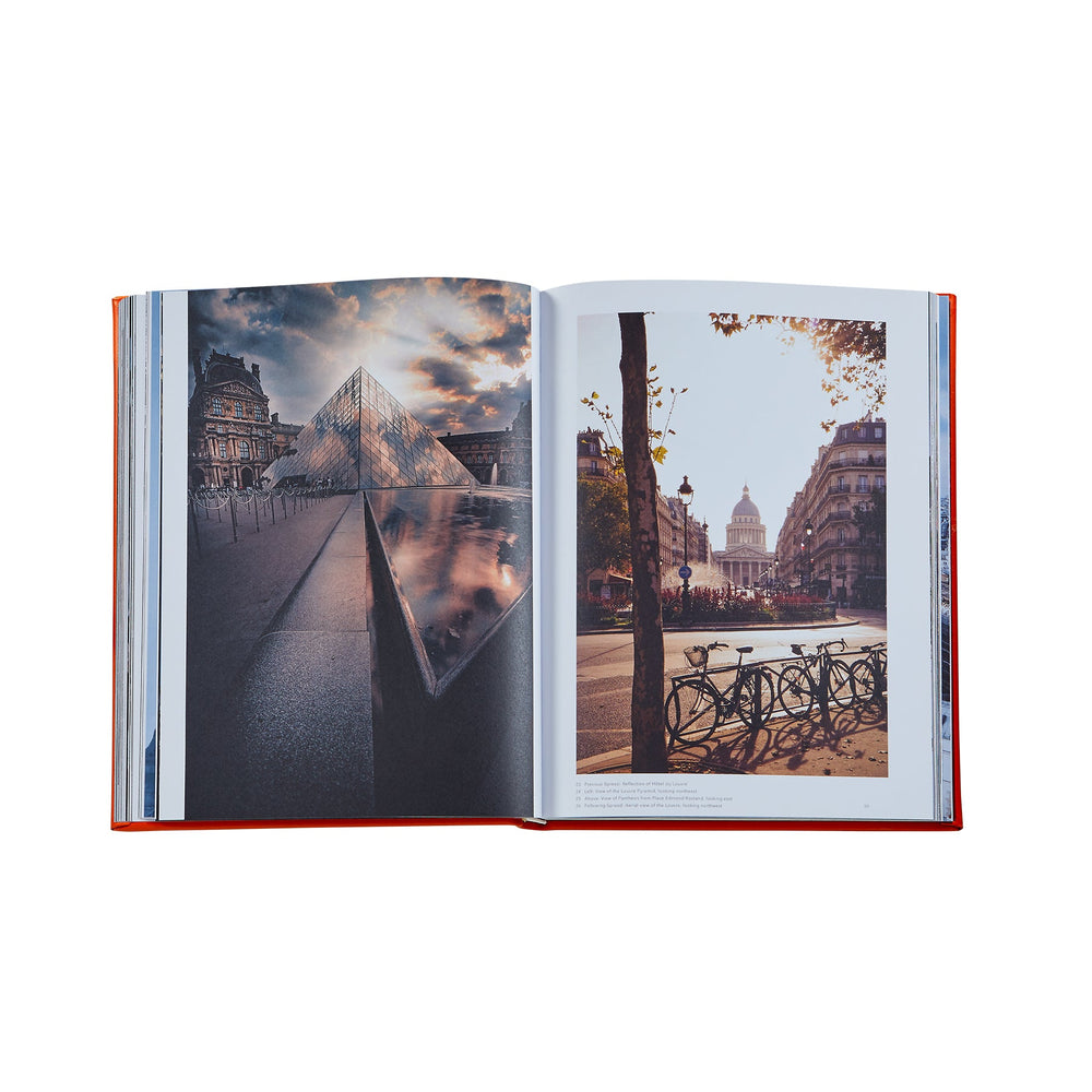 Overhead view of Trope Paris orange leather hardcover book open to two photo spreads showing the Louvre pyramid and a Paris street scene on white background