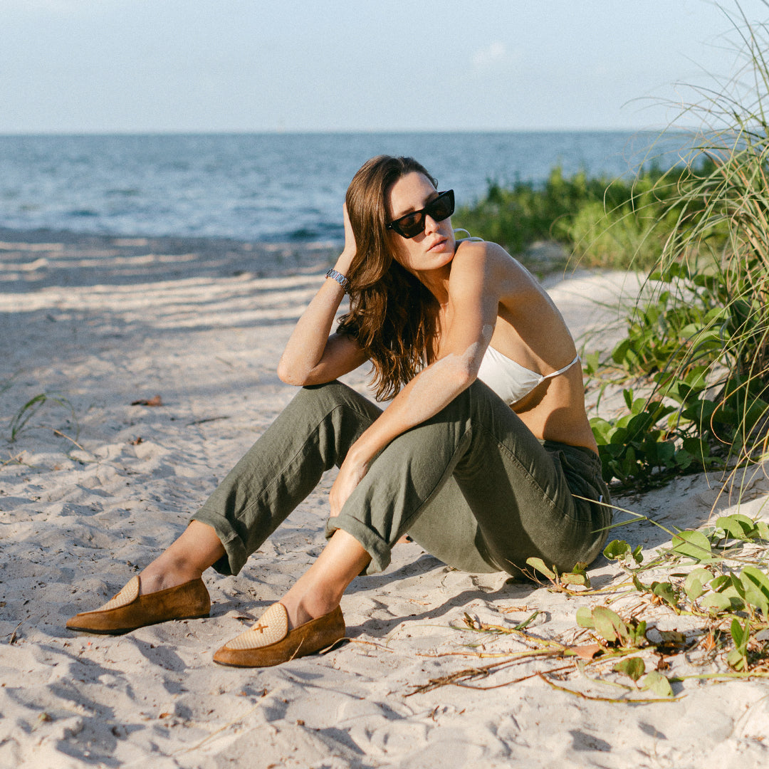 Three quarter view of Women’s Cognac Raffia Milano Loafer showcasing raffia vamp and suede upper on a sandy beach