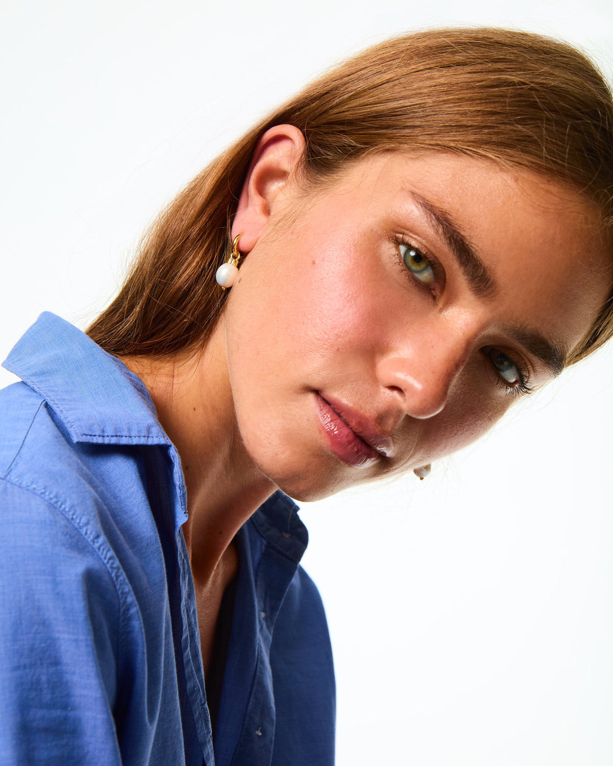 Close-up view of The Pearl Drop Earrings showcasing a freshwater pearl and gold-tone hoop on a model against a white background