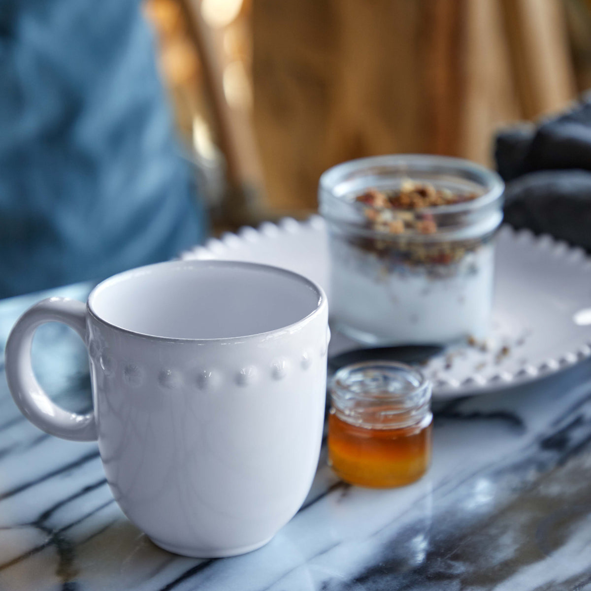 Angled view of Pearl Collection white mug with embossed beaded rim and glossy glaze on marble tabletop