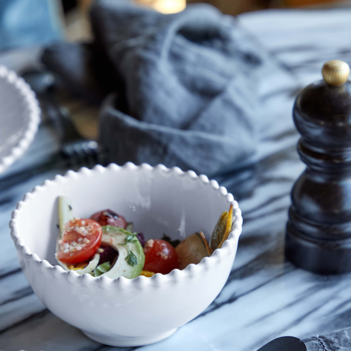 Close-up of Pearl Collection white fruit bowl showing embossed beaded rim and glossy glaze with salad on marble tabletop