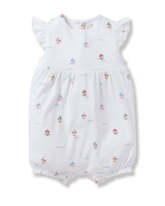 Petite Plumes Babys Pima Isla Play Romper in Bateau is a white romper made from soft Pima cotton, featuring short ruffled sleeves and colorful toy boat patterns. Its slightly puffy design with elastic leg openings offers comfort and style for your little sailor.
