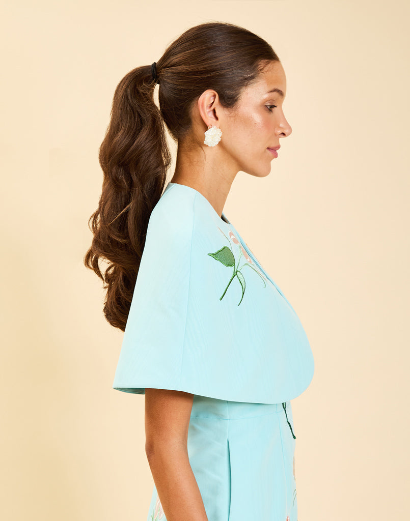 Promenade Embroidered Capelet in Blue Waltz moire with hand-sewn floral embroidery, crew neckline, and hook-and-eye closure.