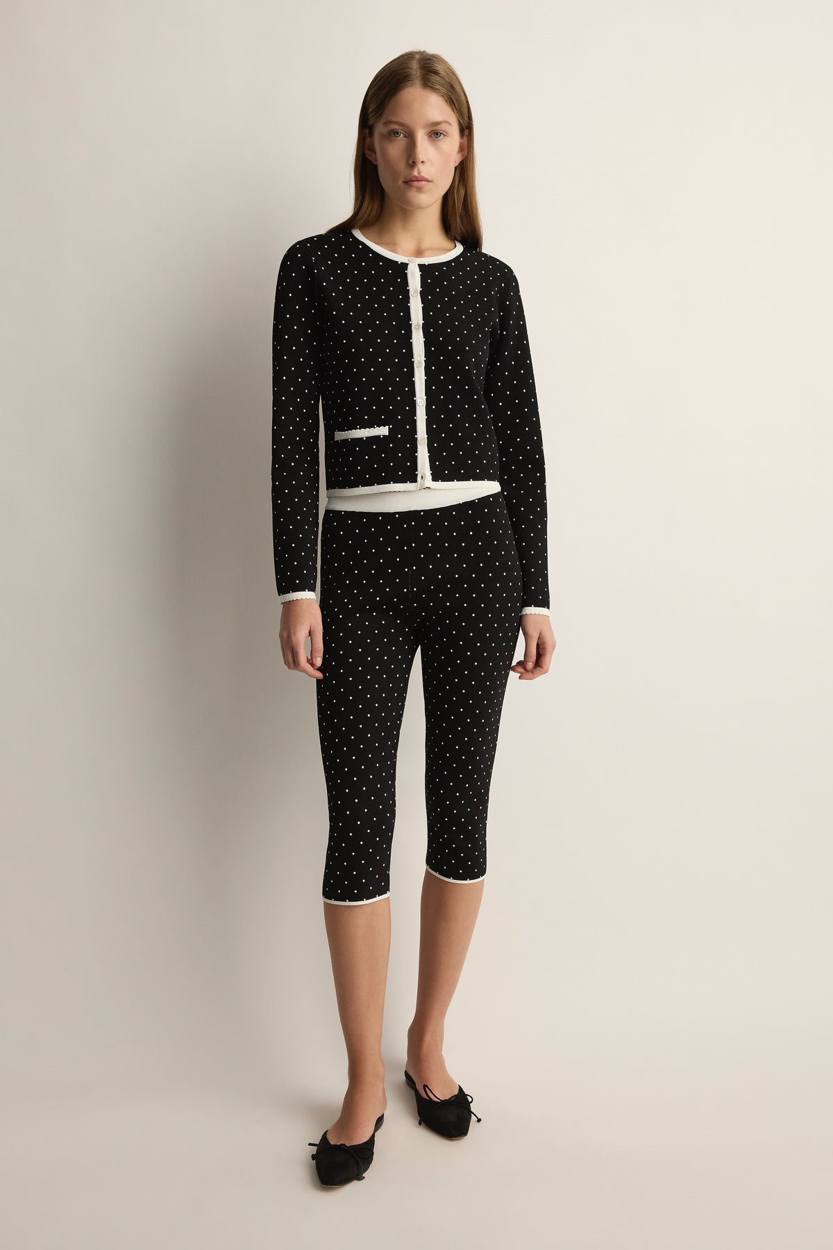 Front view of Michalla cardigan showcasing black and white polka dots, white trim and zip front on a model in a studio