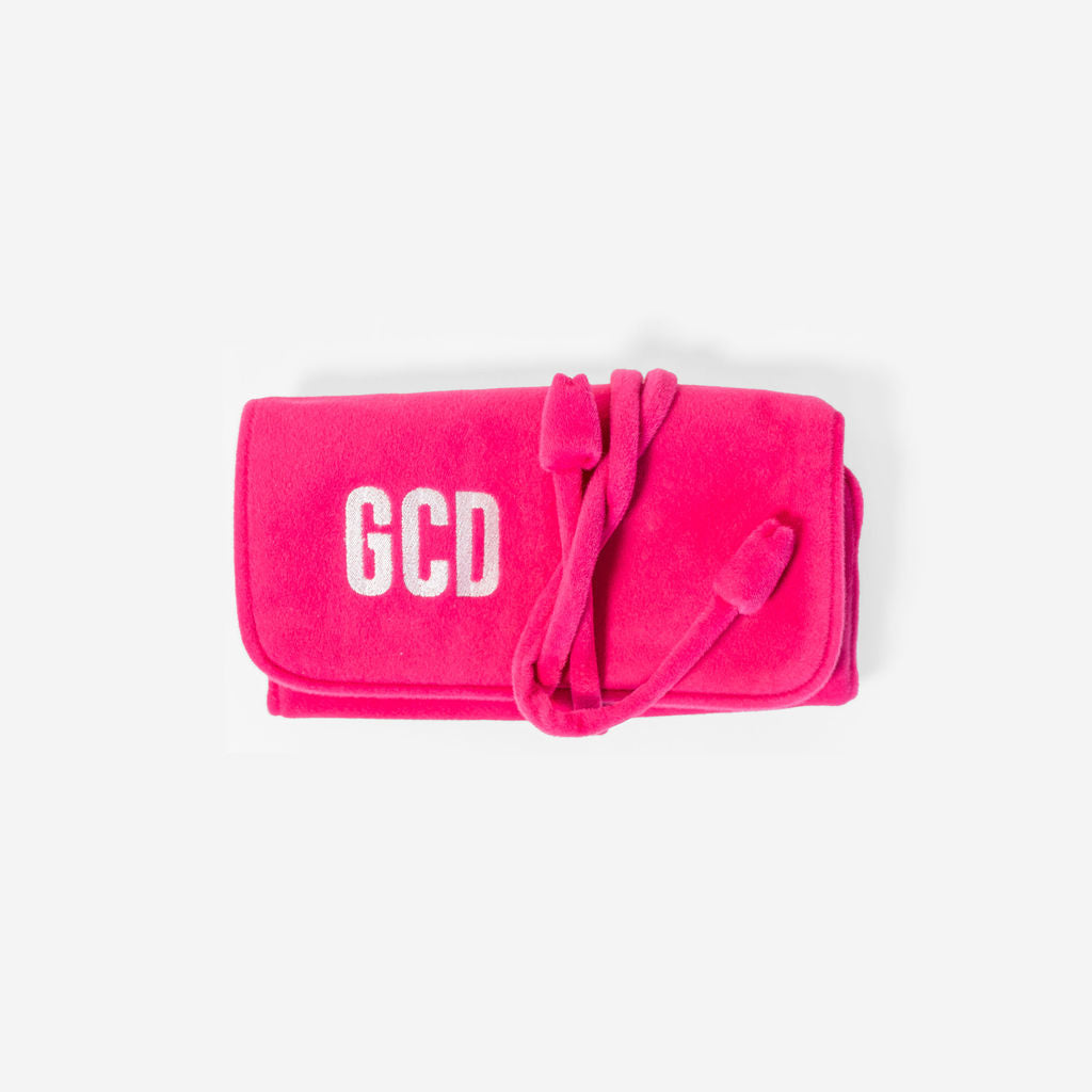 Top view of pink velvet jewelry roll showcasing white GCD monogram and wrap-tie closure on white background