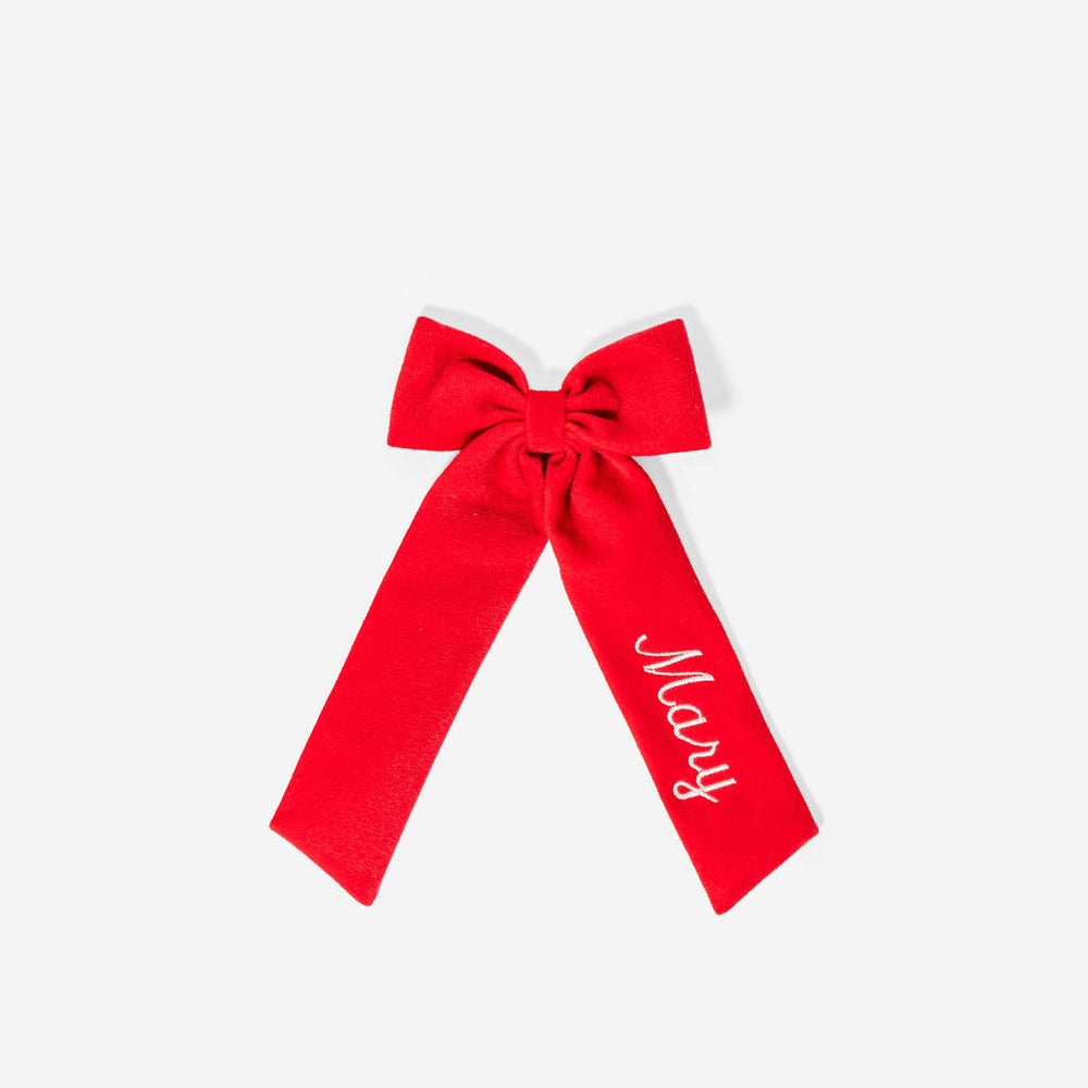 Flat lay of red velvet hair bow with long tails embroidered with script name “Mary” on white background