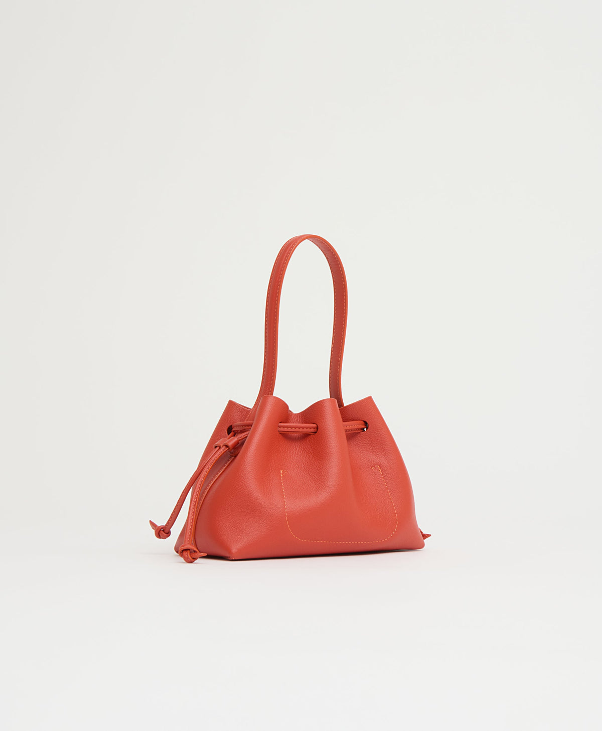 Angled view of Drawstring Pouchette in Pomodoro showing drawstring closure, top handle and pebbled leather on white