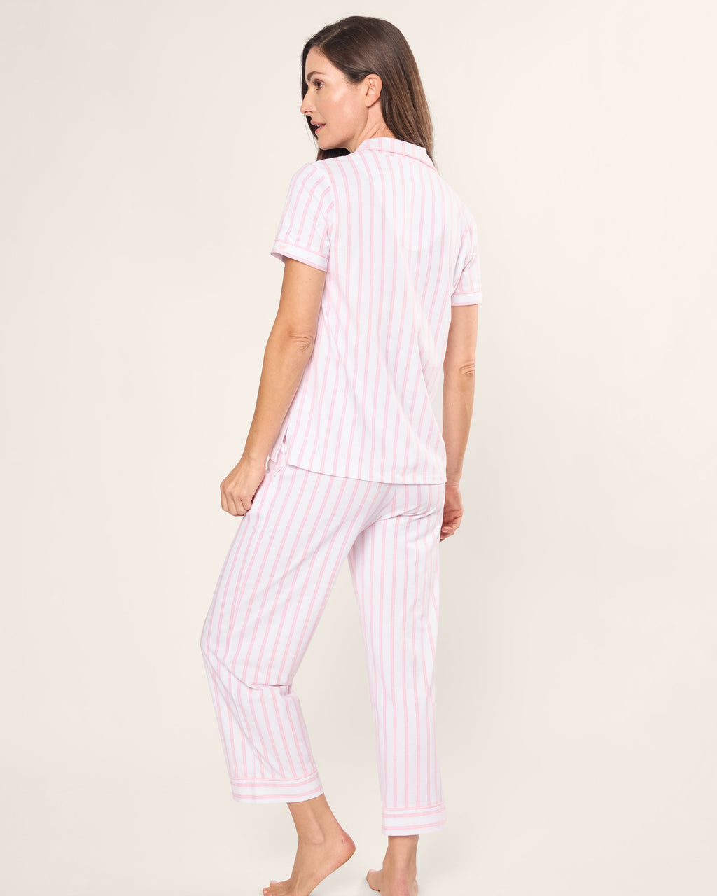 In a Womens Pima Crop Set by Petite Plume, a model stands barefoot against a plain backdrop. This vintage pajama set, featuring pink and white striped short-sleeve top and pants, is made from soft Pima cotton for ultimate comfort.