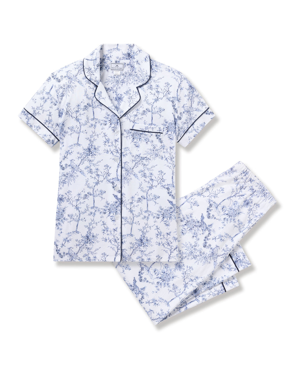 The Womens Pima Crop Set in Timeless Toile by Petite Plume showcases botanical elegance with short sleeves, a white backdrop, and blue floral design. It features a button-up shirt with a chest pocket and matching pants, both outlined with dark piping for classic sophistication.