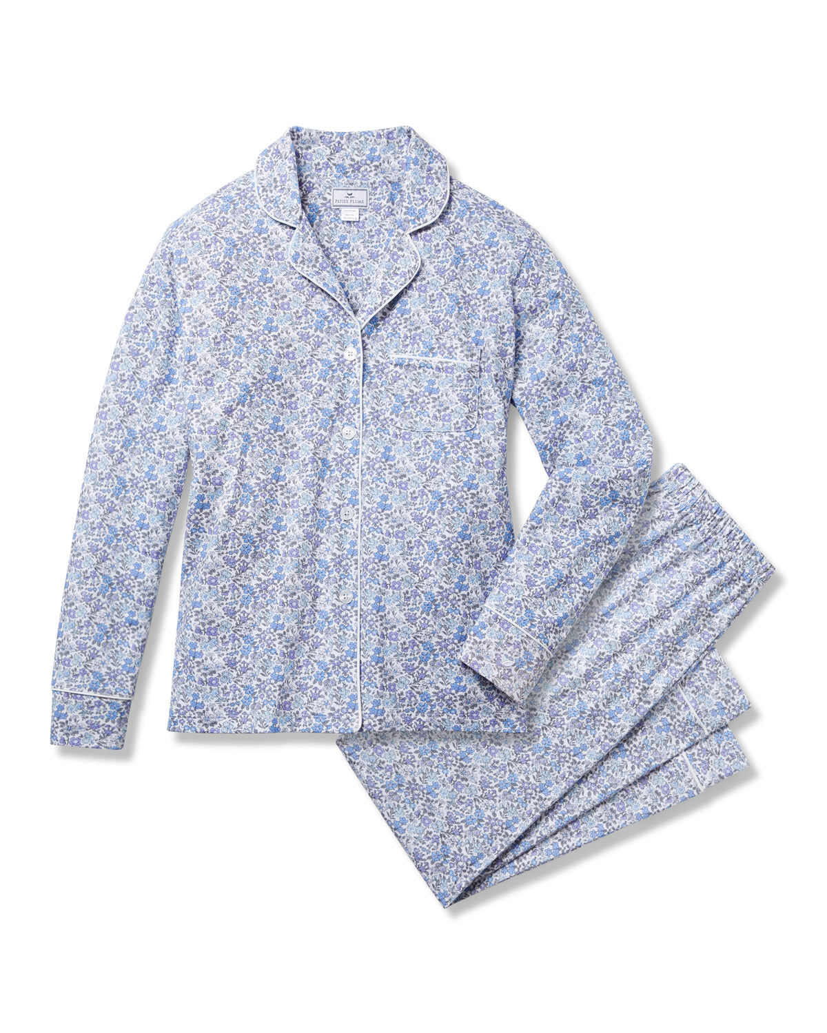 The Womens Pima Pajama in Fleur dAzur by Petite Plume is a vintage-inspired set with blue floral patterns, crafted from luxurious Peruvian Pima cotton. It features a long-sleeve button-up shirt with a chest pocket and matching pants, accented by white piping on the collar, cuffs, and pocket edges.