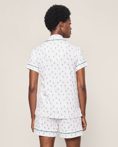 A person with short curly hair is shown from the back wearing Petite Plumes Womens Pima Short Sleeve Short Set in Palmier, made of Peruvian Pima cotton, featuring a small green plant pattern and green-trimmed edges. The background is plain beige.
