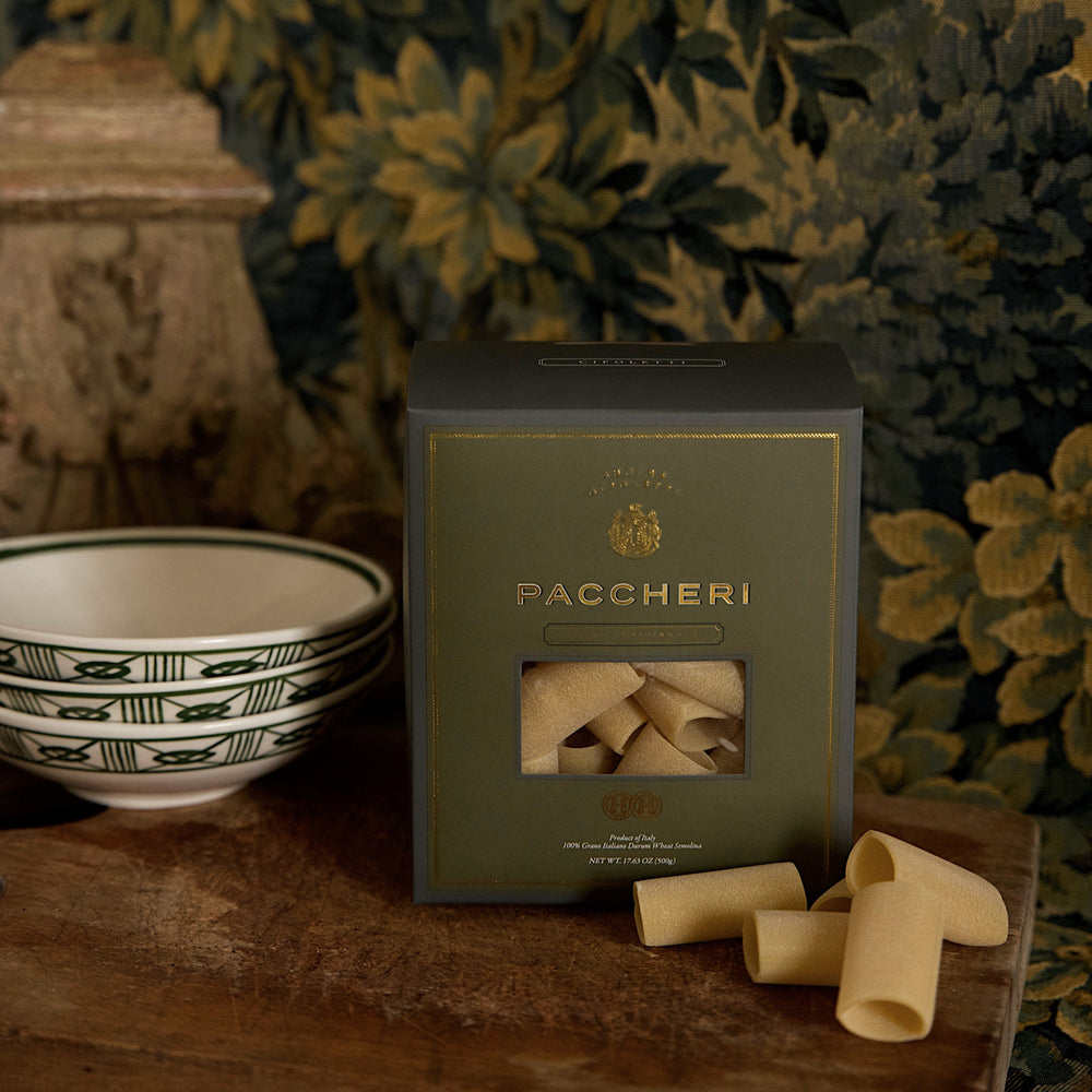 Front view of Paccheri box with gold embossed lettering and window showing pasta tubes on a wooden table and bowls