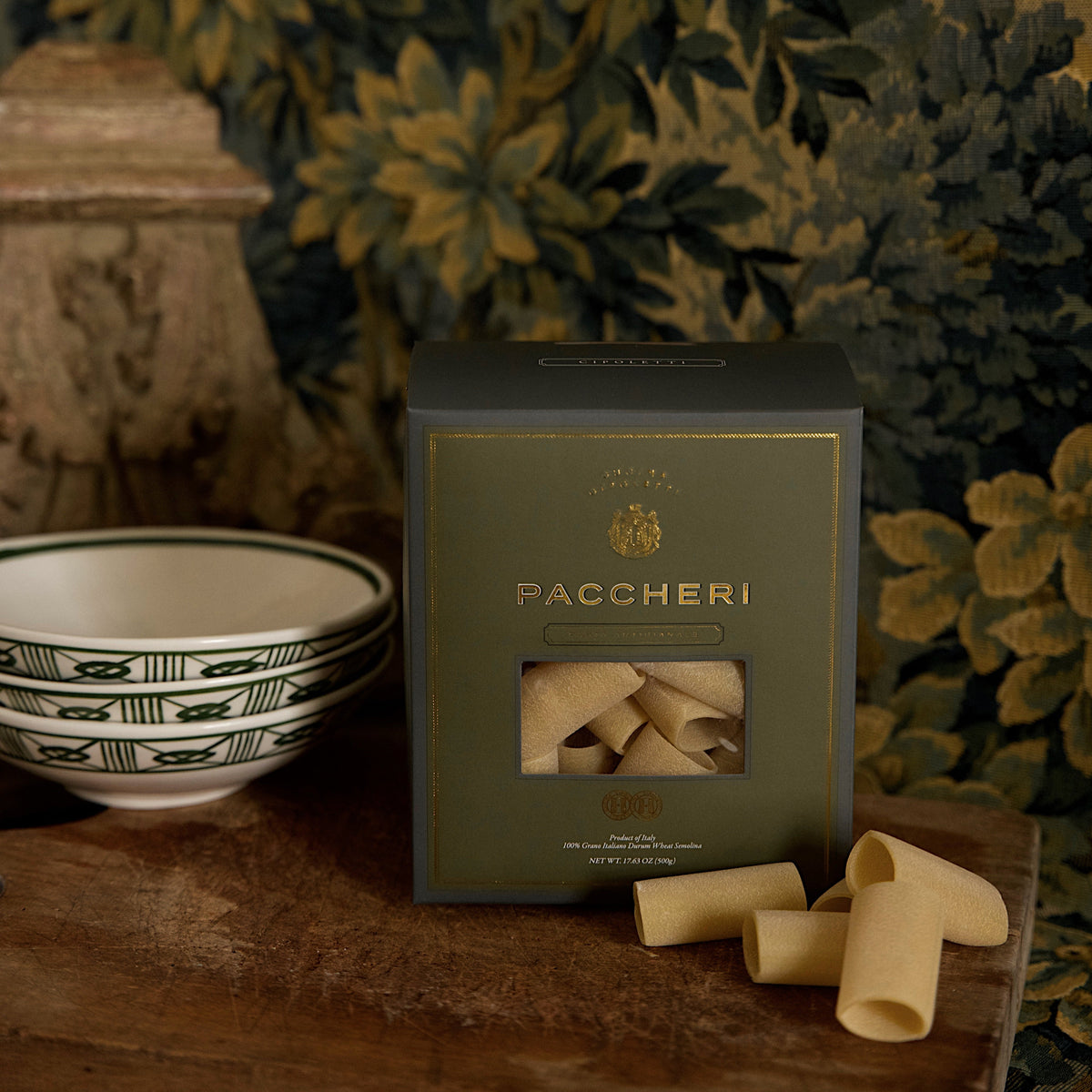 Front view of Paccheri box with gold embossed lettering and window showing pasta tubes on a wooden table and bowls