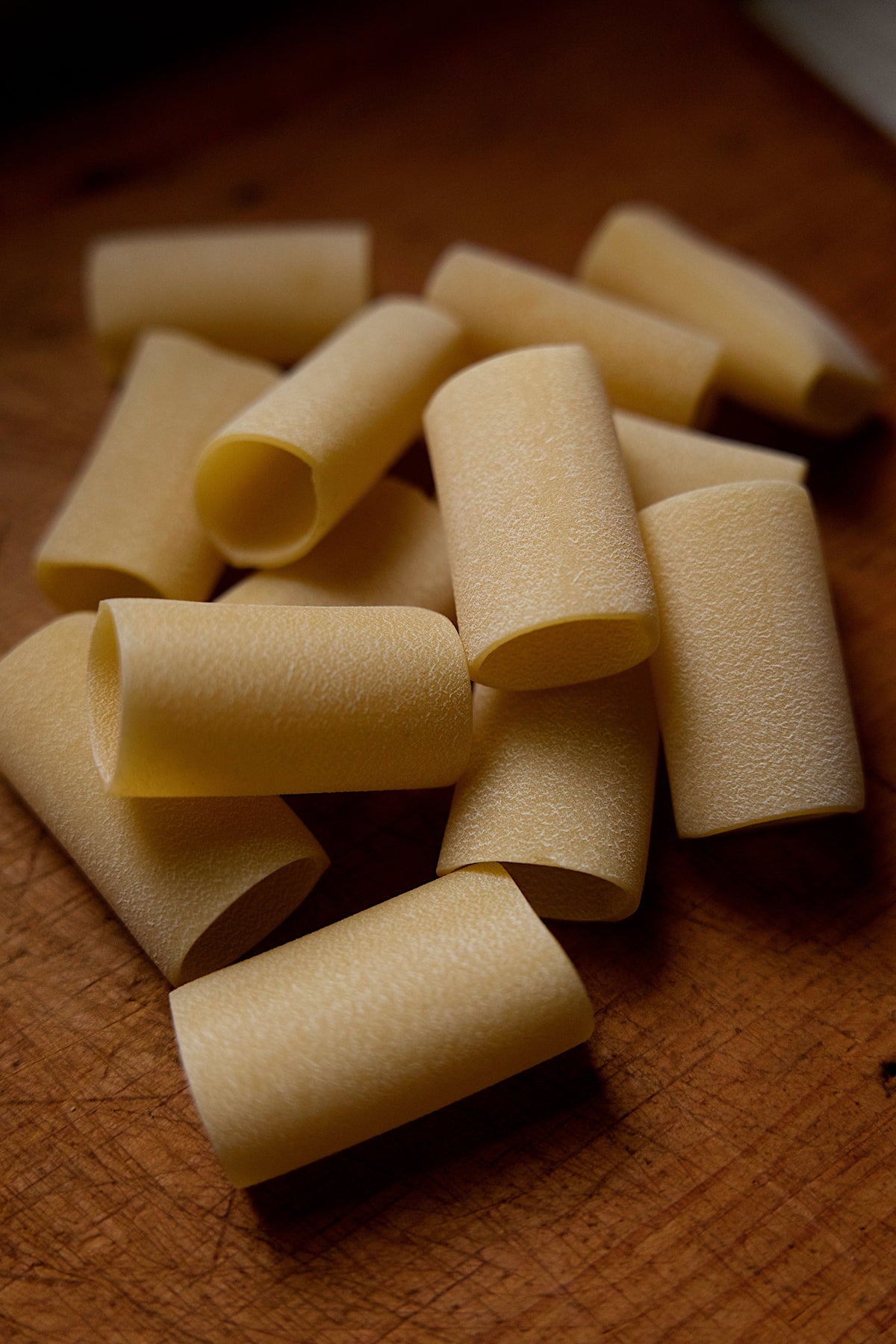 Close-up of uncooked Paccheri Bronze cut Pasta tubes on a wooden surface.