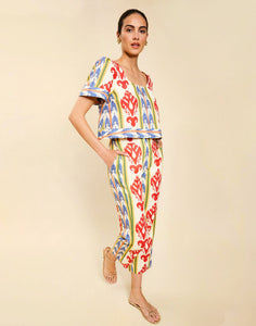 Woman wearing the Mestiza Palau Cigarette Pant in Ikat Sunrise print, featuring a slim-fit cigarette silhouette, front pleat detailing, cropped ankle-length fit, and lightweight linen fabrication.