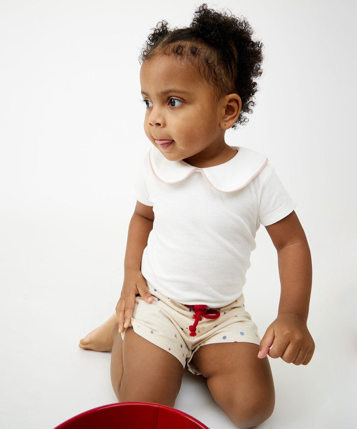 Three-quarter view of Pan One-Piece in Rose Piping on seated toddler, showing short sleeves and Peter Pan collar
