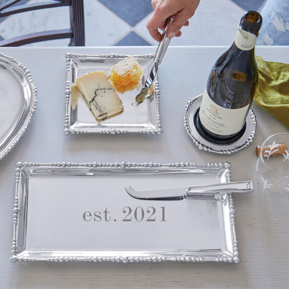 Top view of Signature Cheese Knife Set with stainless steel blades and beaded silver trays engraved est 2021 on a light table