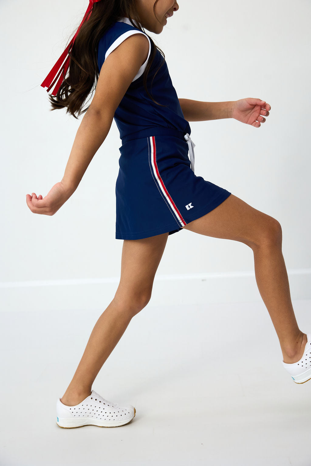 Side view of Liberty Love skort in navy showcasing built-in shorts, drawstring waist, and red-white side stripe against white background