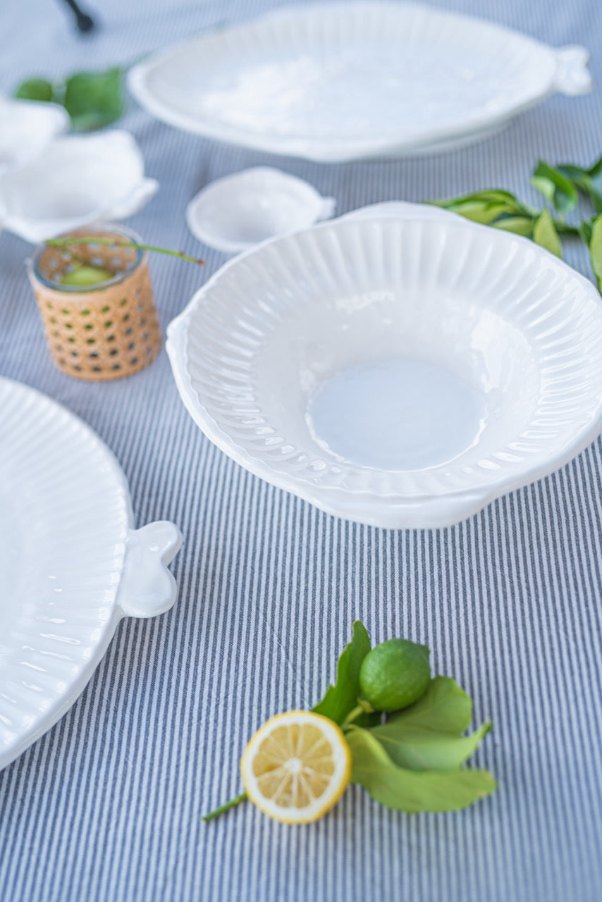Angled view of Pesce Serena cereal bowl showing fluted scalloped rim and fish handle on blue-striped tablecloth with lemon