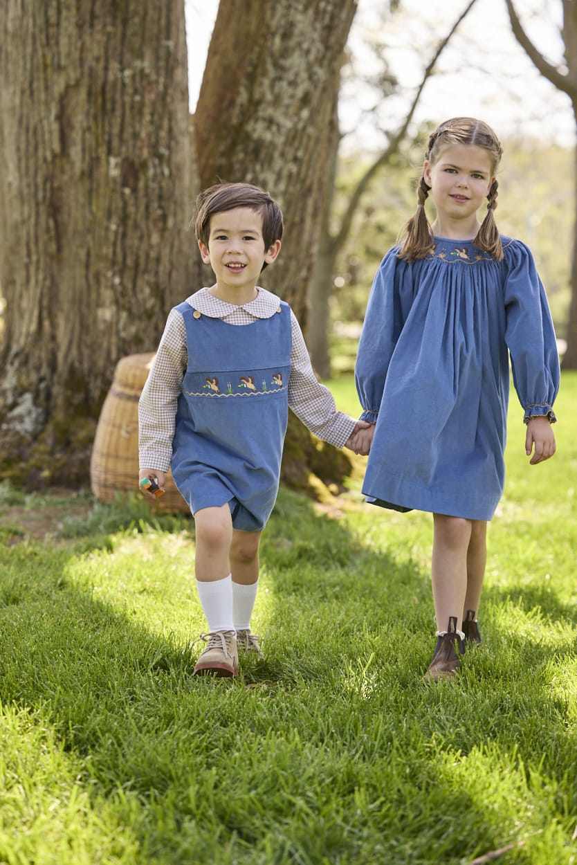 Little English traditional children's clothing.  Khaki Gingham peter pan shirt for toddler boys paired with stormy blue corduroy shortall with flying mallard smocking across chest. Long sleeve stormy blue corduroy dress with flying mallard collar around the neckline for little girls.