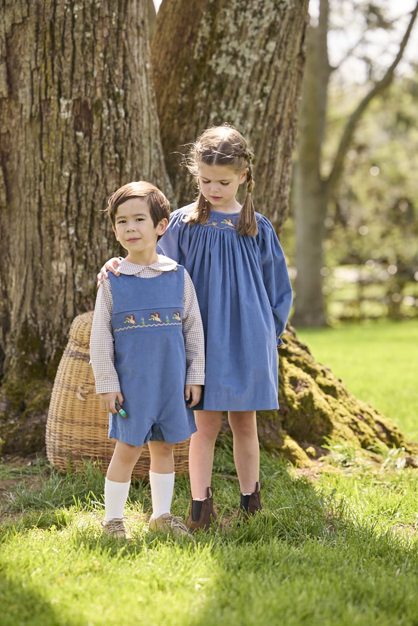 Little English traditional children's clothing.  Khaki Gingham peter pan shirt for toddler boys paired with stormy blue corduroy shortall with flying mallard smocking across chest. Long sleeve stormy blue corduroy dress with flying mallard collar around the neckline for little girls.