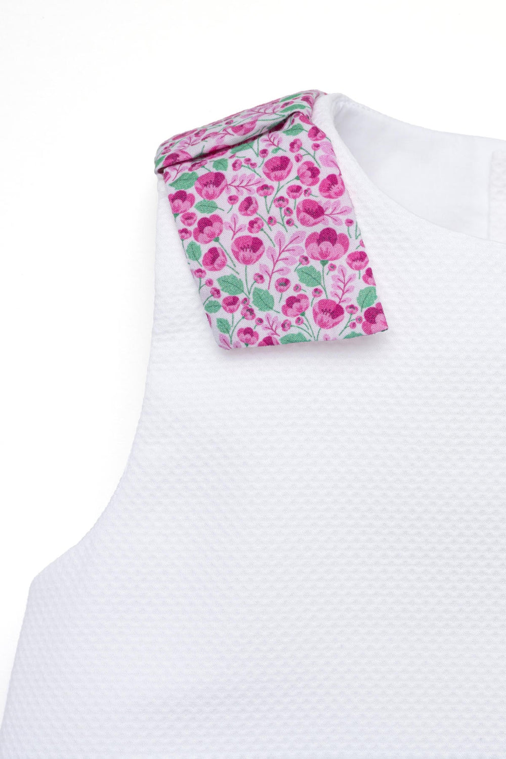 Close up of Sofia baby set shoulder showing Radiant Poppies floral shoulder tab and white textured bodice on white background