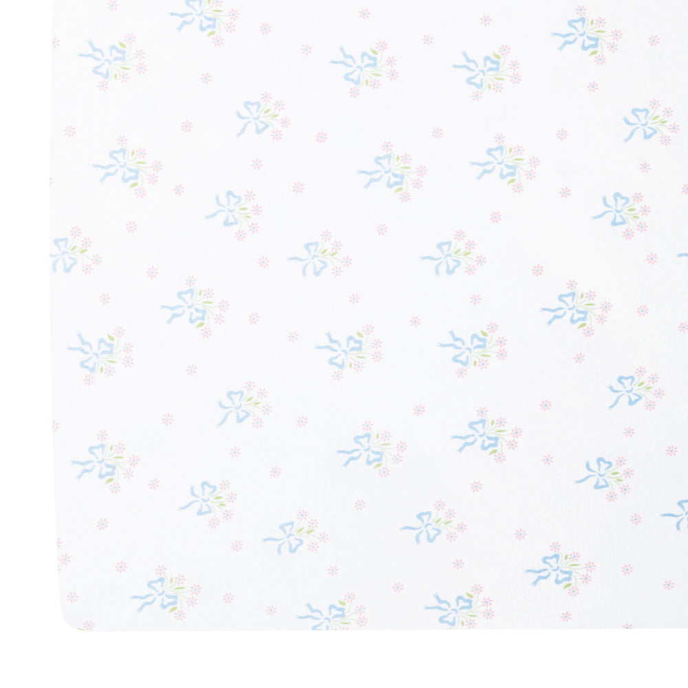 Top-down view of Pima crib sheet showing blue bow-tied pink floral bouquet all-over print on white background