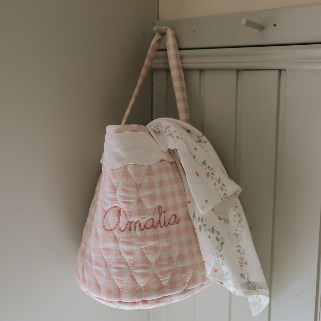 Quilted baby bag with 'Amalia' embroidery hanging on a wardrobe door.