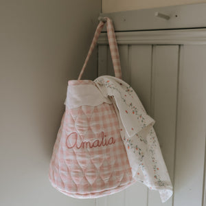 Quilted baby bag with 'Amalia' embroidery hanging on a wardrobe door.