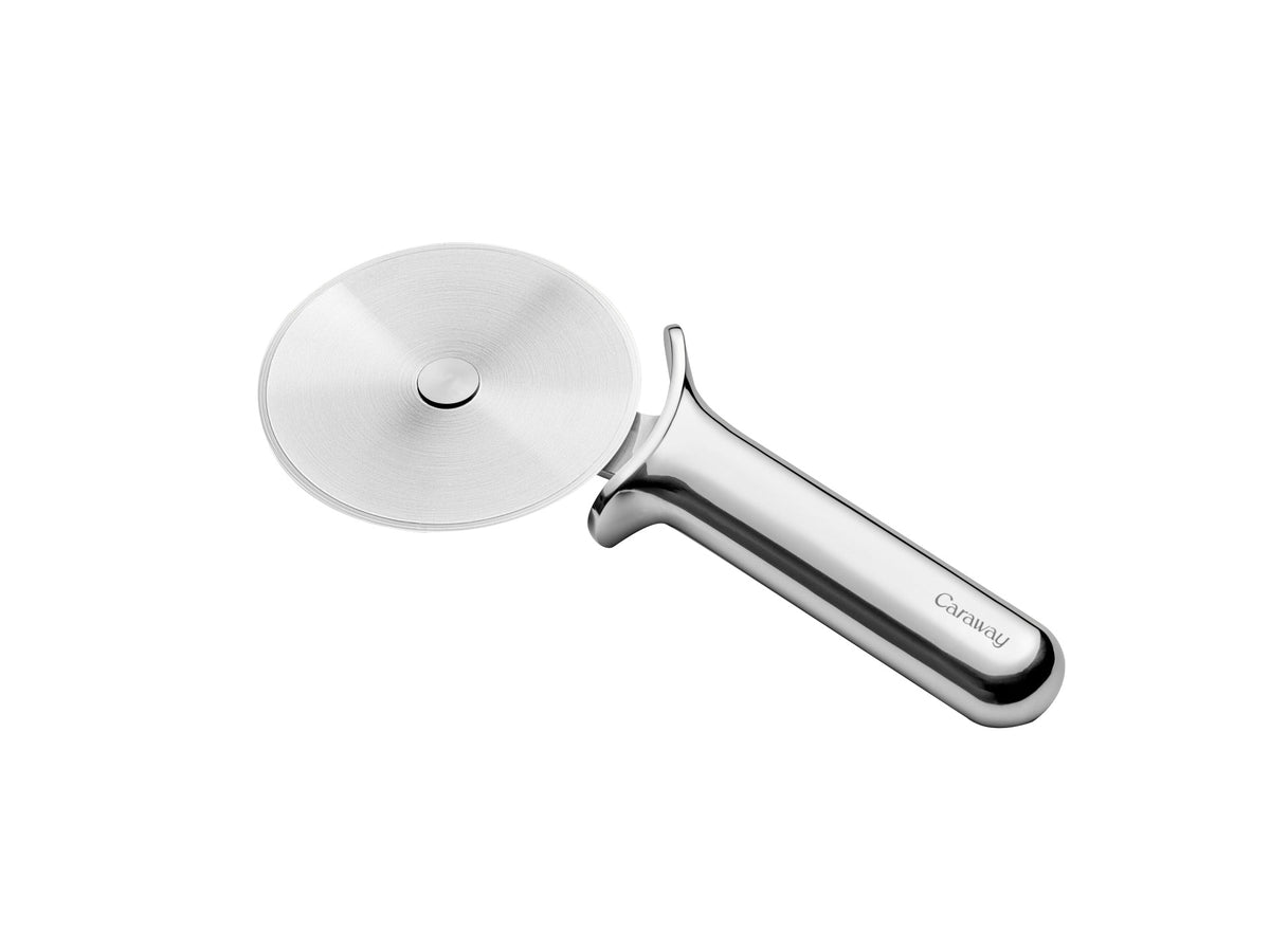 Angled top view of Caraway pizza cutter showcasing stainless steel rotating blade and ergonomic polished handle on white background