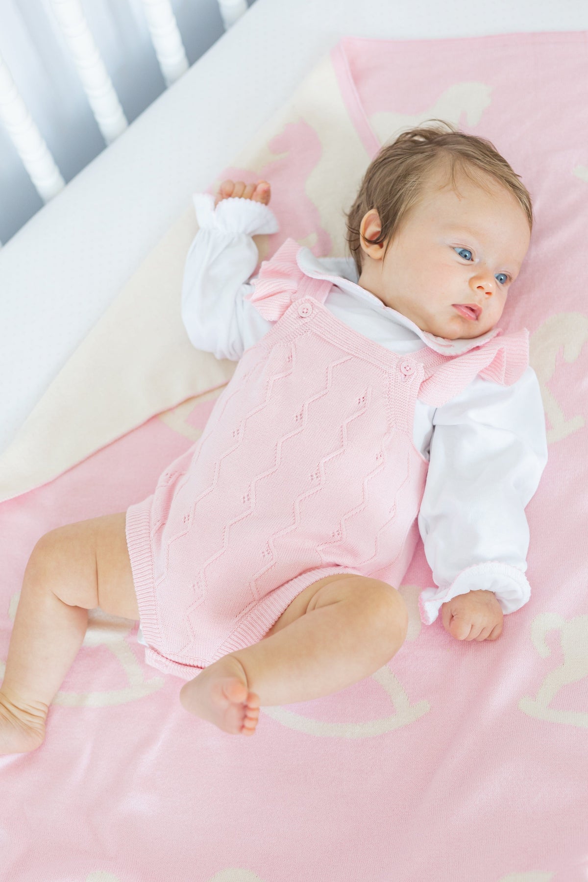 Overhead of pink Rocking Horse nursery blanket showing cream rocking horse motif with baby in white crib
