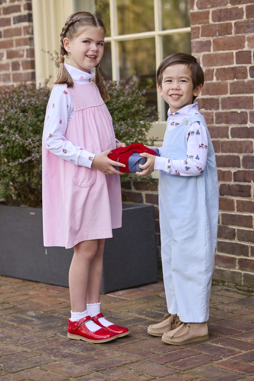 Little English classic children's clothing. White knit turtleneck with holiday train print layered under light blue corduroy Campbell Overall. White knit turtleneck with holiday present print layered under light pink corduroy Madison Jumper. Holiday outfit for little boys and girls.