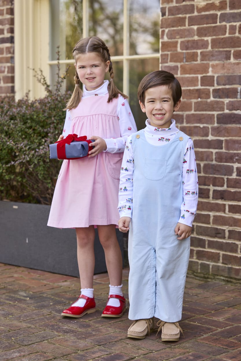 Little English classic children's clothing. White knit turtleneck with holiday train print layered under light blue corduroy Campbell Overall. White knit turtleneck with holiday present print layered under light pink corduroy Madison Jumper. Holiday outfit for little boys and girls.
