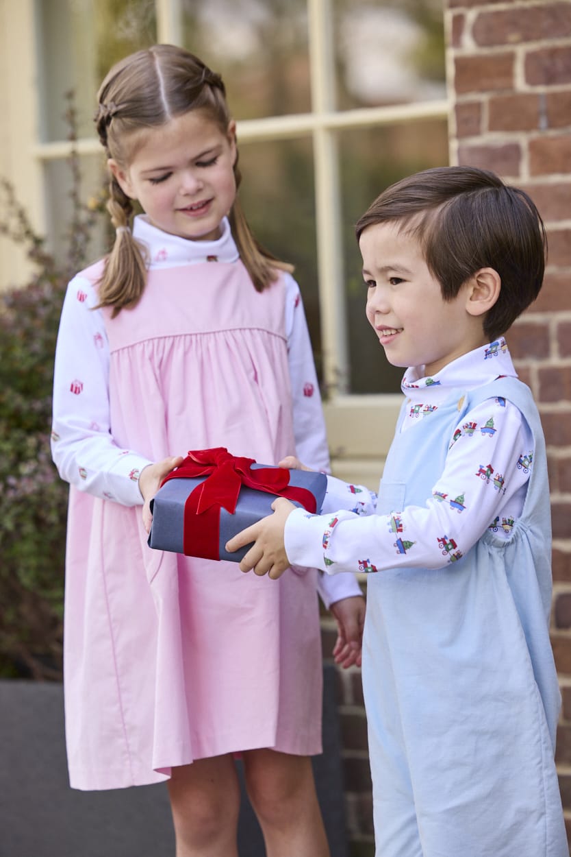 Little English classic children's clothing. White knit turtleneck with holiday train print layered under light blue corduroy Campbell Overall. White knit turtleneck with holiday present print layered under light pink corduroy Madison Jumper. Holiday outfit for little boys and girls.